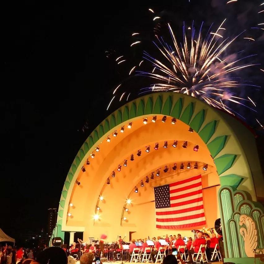 Fireworks going off over an outdoor stage with an American flag in the background