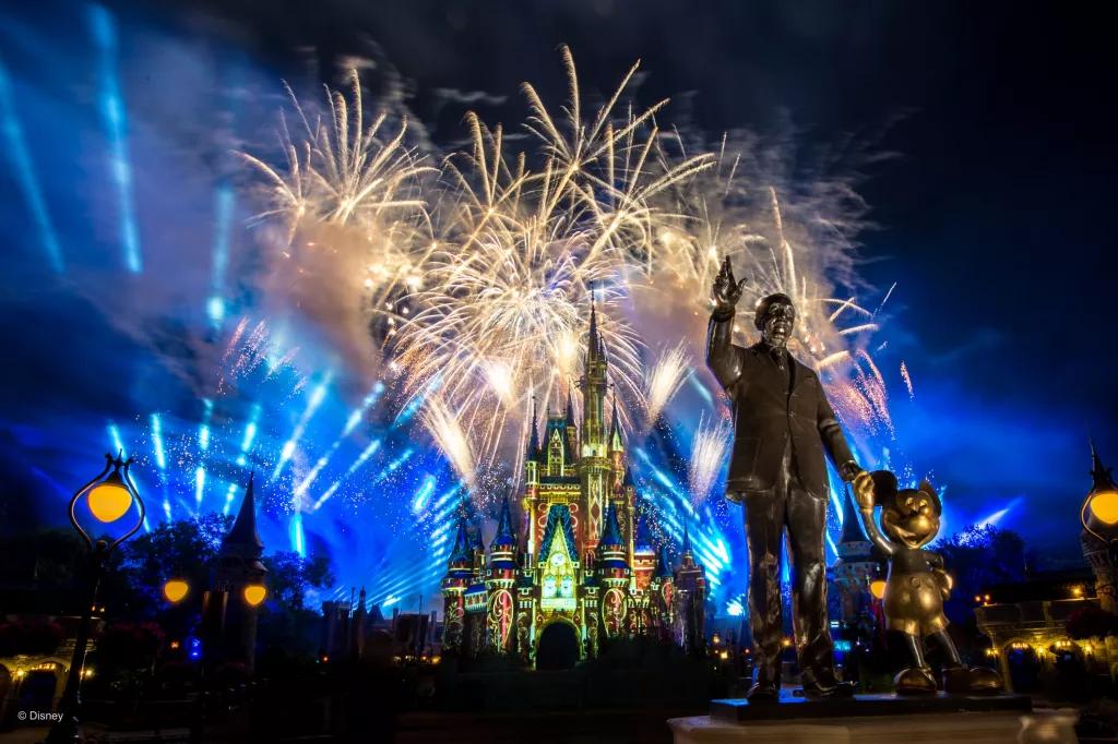 Fireworks going off over Cinderella Castle at Magic Kingdom behind a statue of Walt Disney and Mickey Mouse