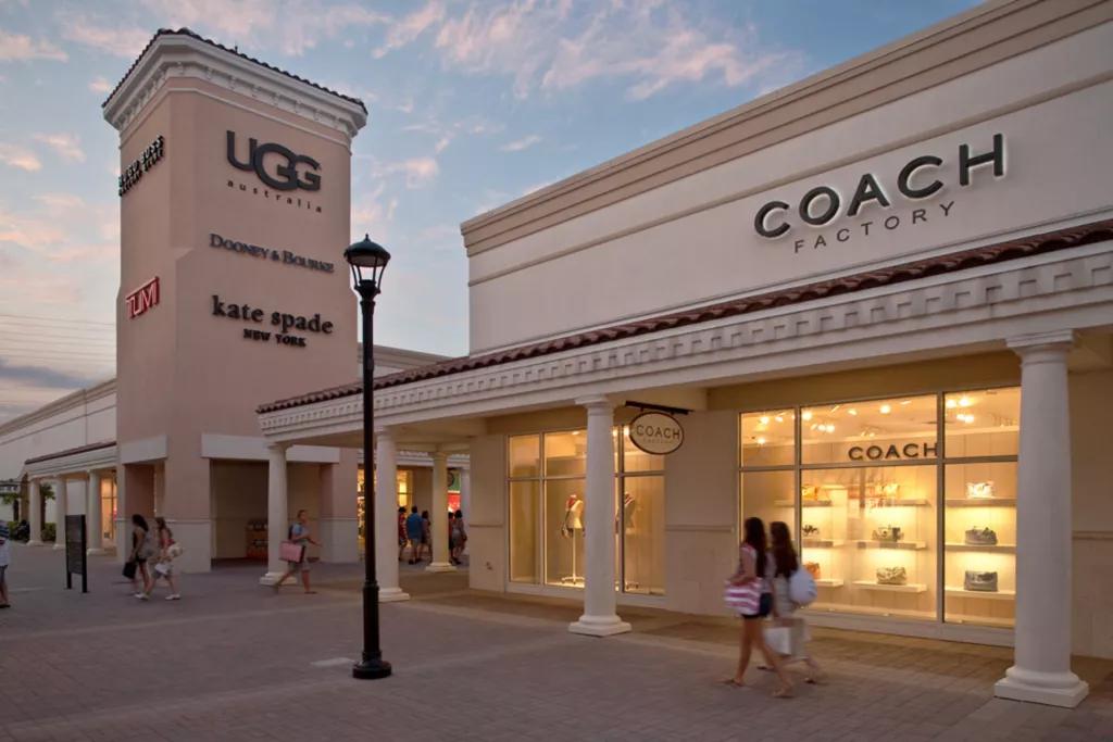 The exterior of a Coach outlet store with two people walking outside