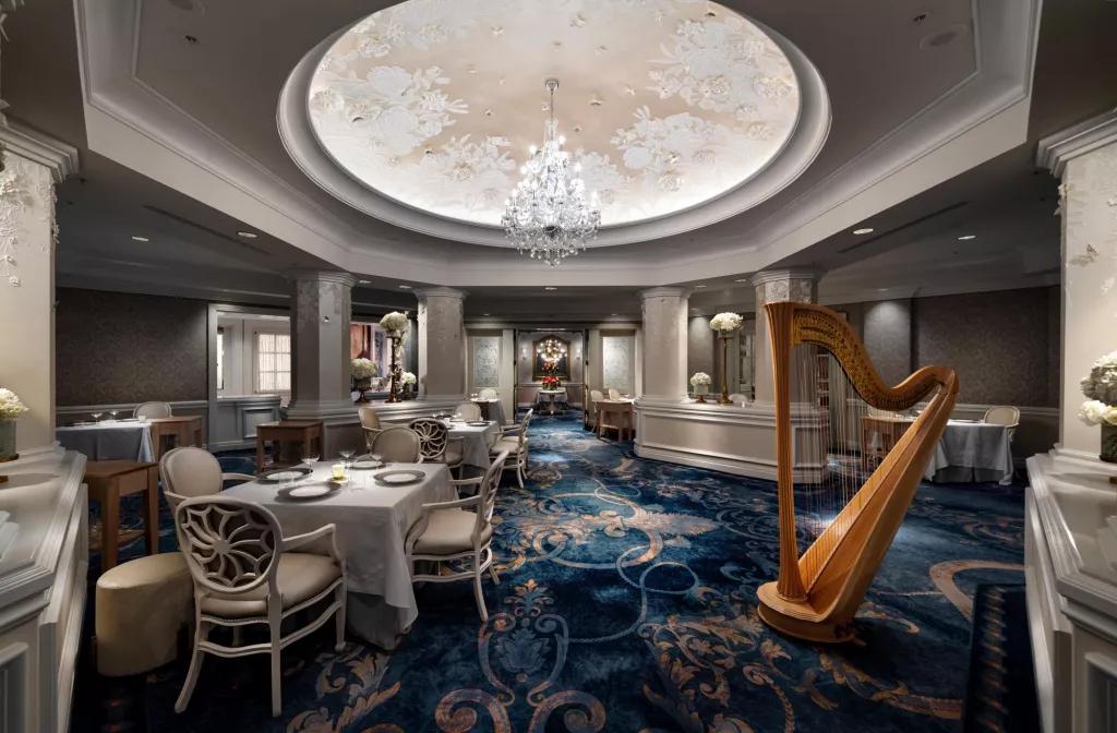 The interior of a restaurant with a chandelier hanging from the ceiling and a harp next to some white tables and chairs