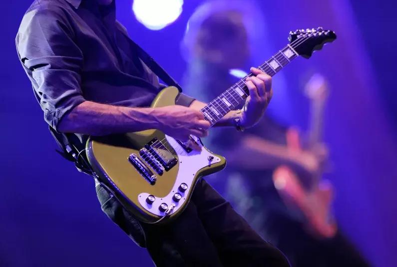 The mid section of a man on stage playing a guitar