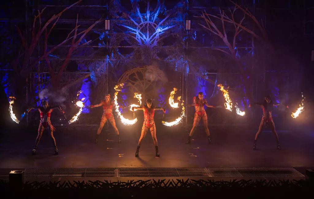 Performers on a dark stage wearing leotards and twirling batons of fire