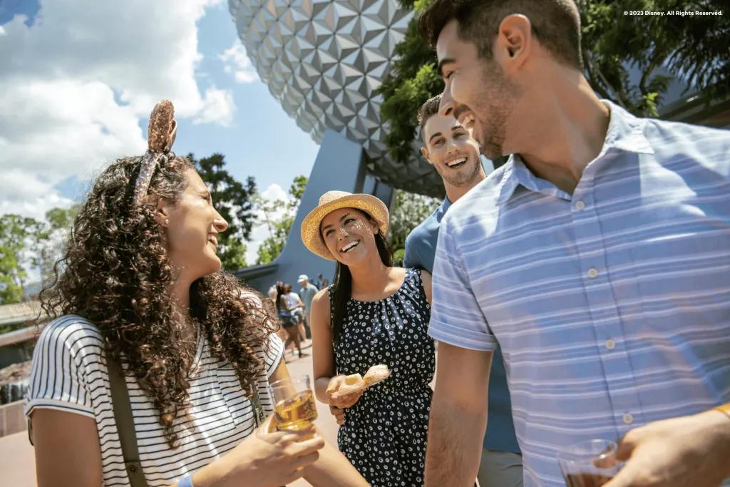 Two men and two women laughing while eating and drinking in front of Spaceship Earth