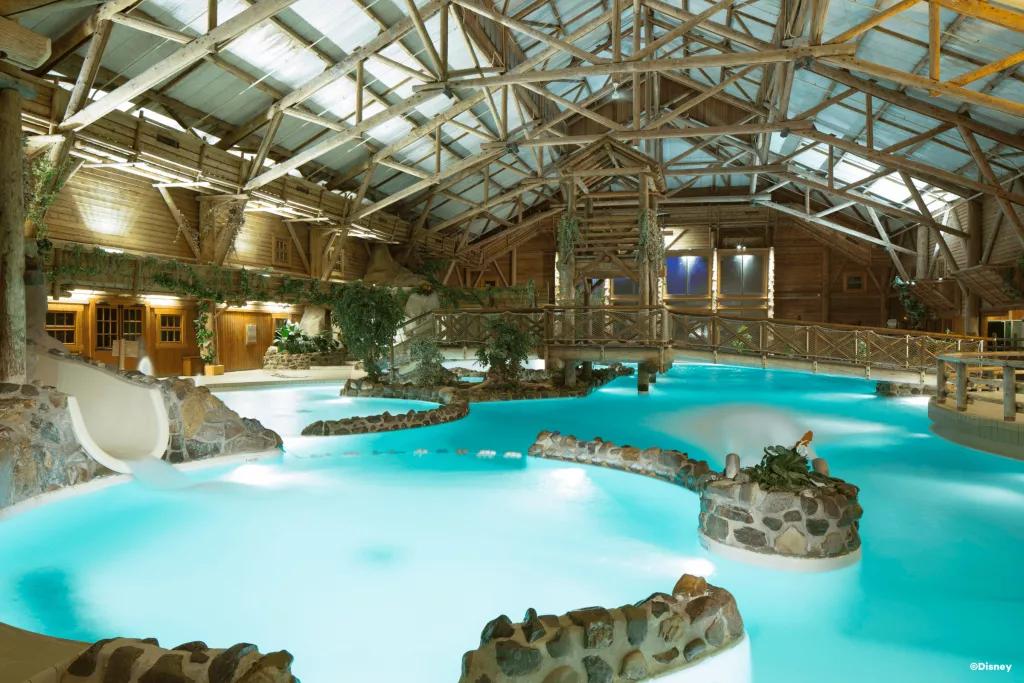 An indoor pool decorated with rocks, greenery and wooden accents