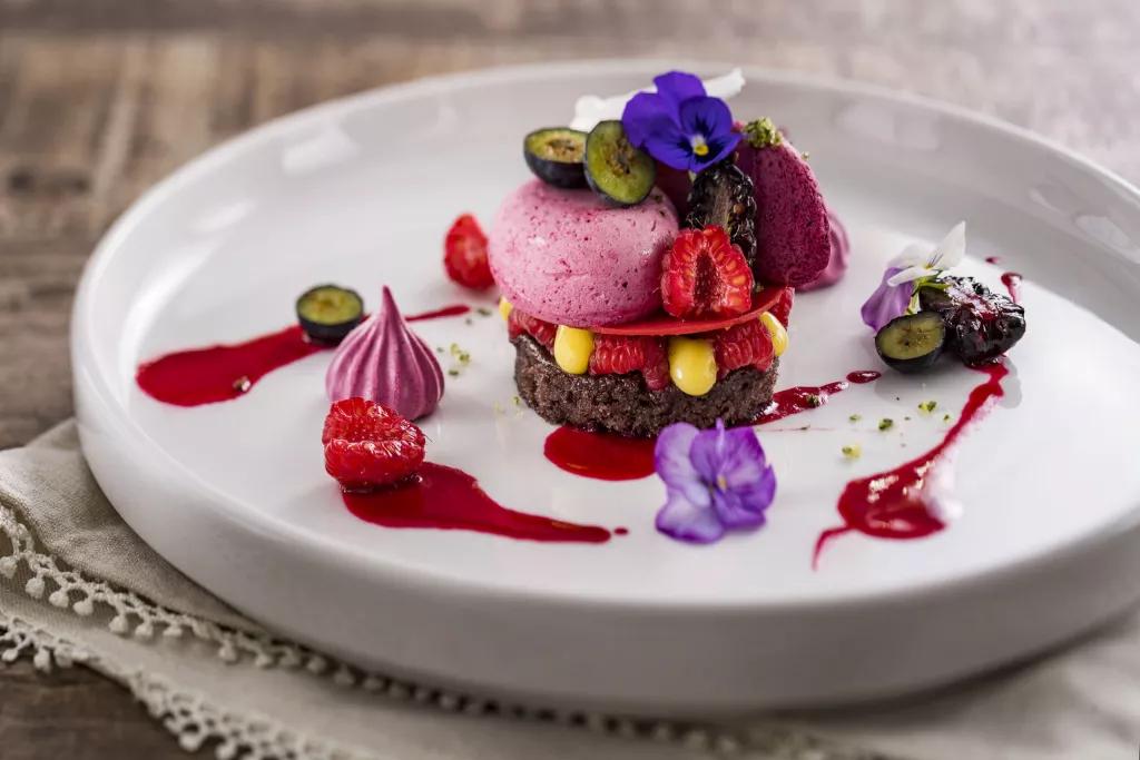 A chocolate dessert topped with fruit, meringue and flowers