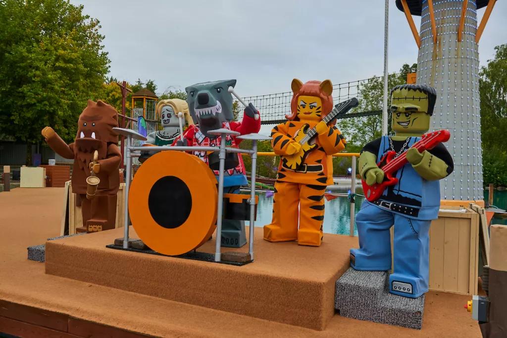 People wearing Lego monster costumes standing on a stage playing pretend instruments