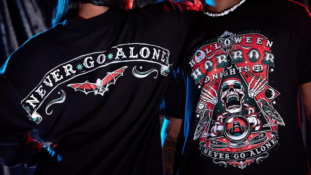 A woman facing away from the camera wearing a shirt that reads 'Never Go Alone' and a man facing the camera wearing a tshirt reading 'Halloween Horror Nights'