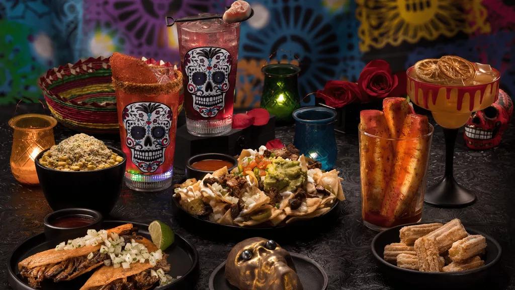 A table full of food including nachos, tacos, churros, candy skull cocktails and a cake shaped like a skull