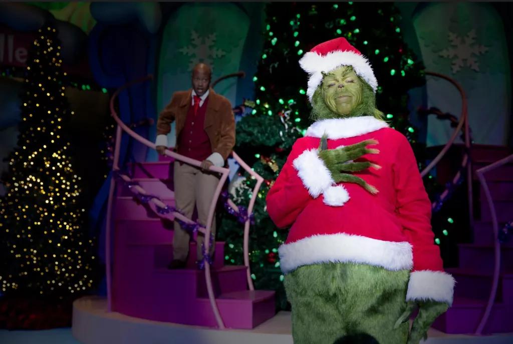 The Grinch dressed as Santa standing with his hand on his heart