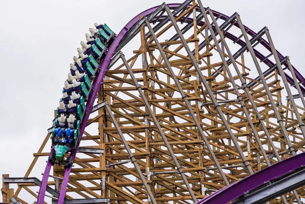 A teal coloured rollercoaster car going down a slope on a hybrid wood and steel coaster