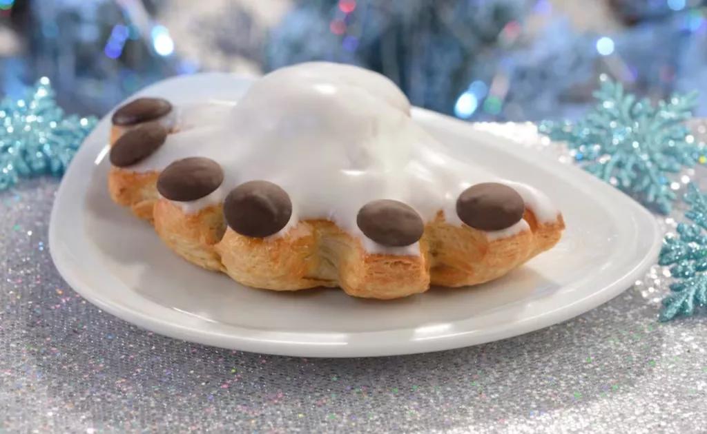 A pastry covered in icing and decorated with chocolate on a silver tinsel covered table