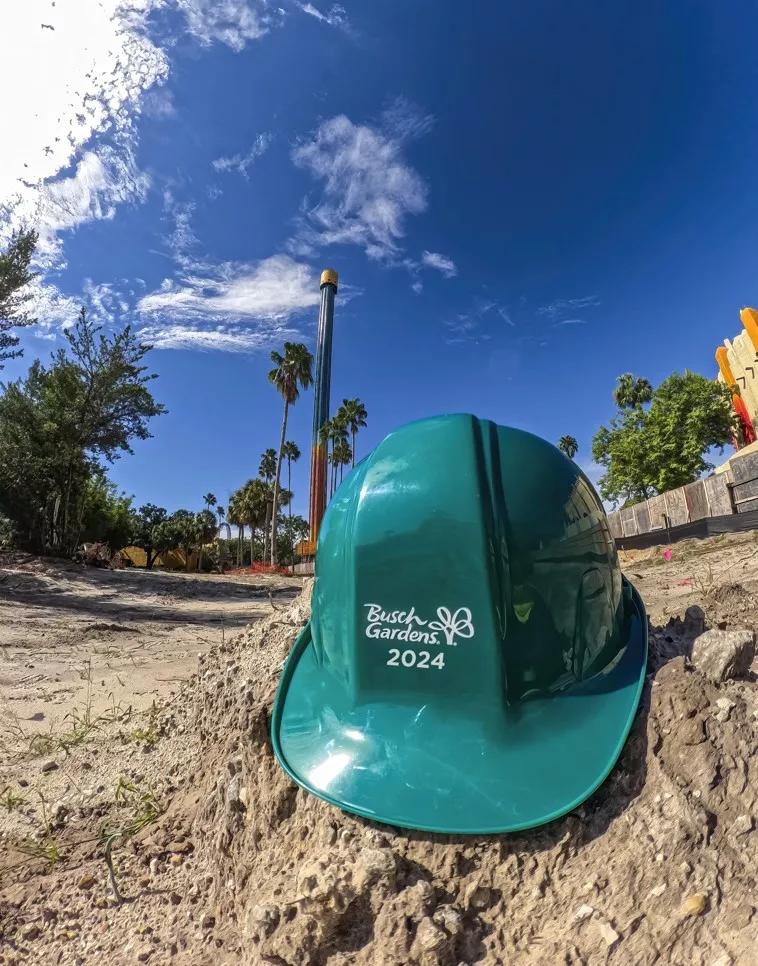 A teal hard hat with Busch Gardens 2024 printed on it in white text sitting on some sand