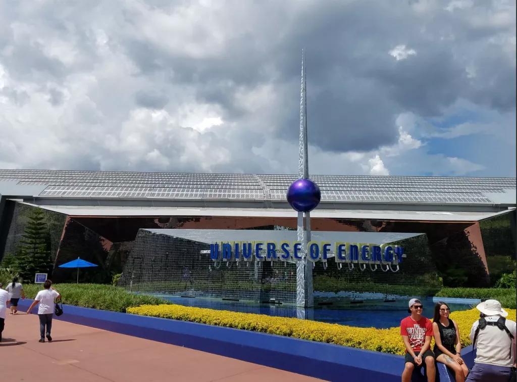 Two people getting their picture taken outside of a mirrored building with a sign reading Universe of Energy