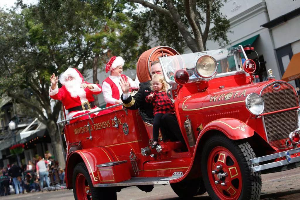 A man and child riding in a red old-fashioned fire truck with Santa and Mrs Clause in the back
