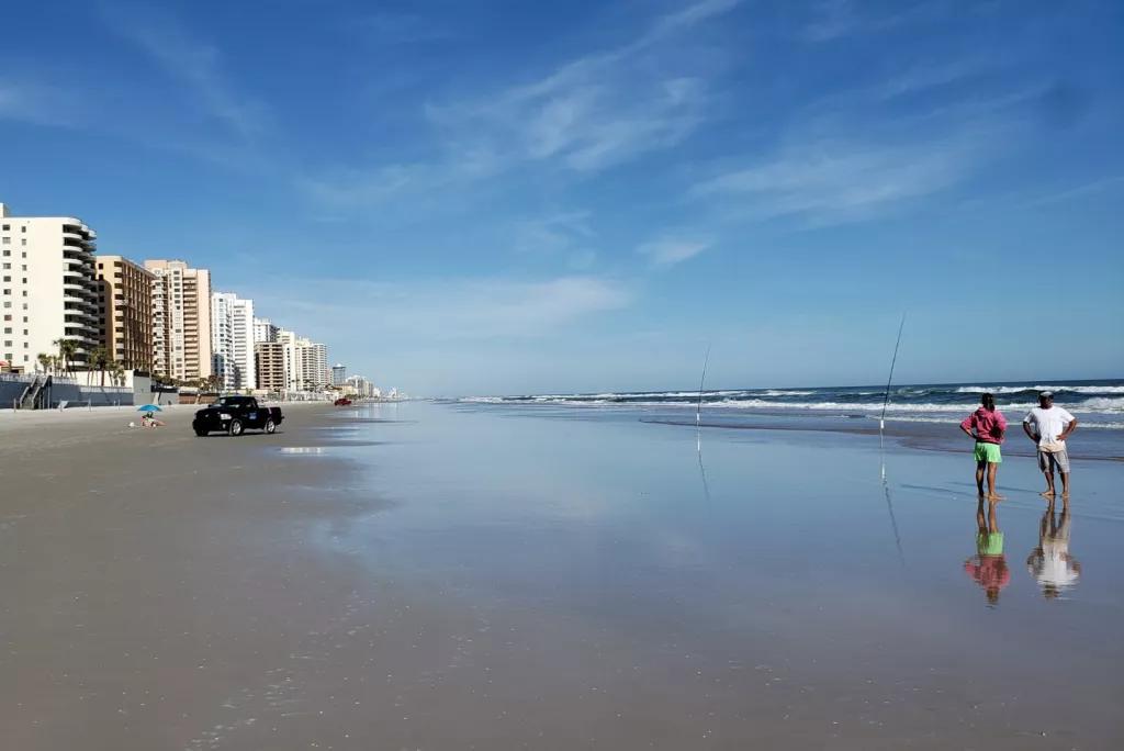 People standing on the shore of a quiet beach in front of a bright blue sky