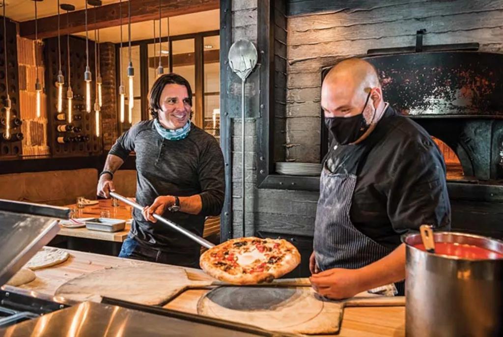 Two men serving a pizza onto a wooden board