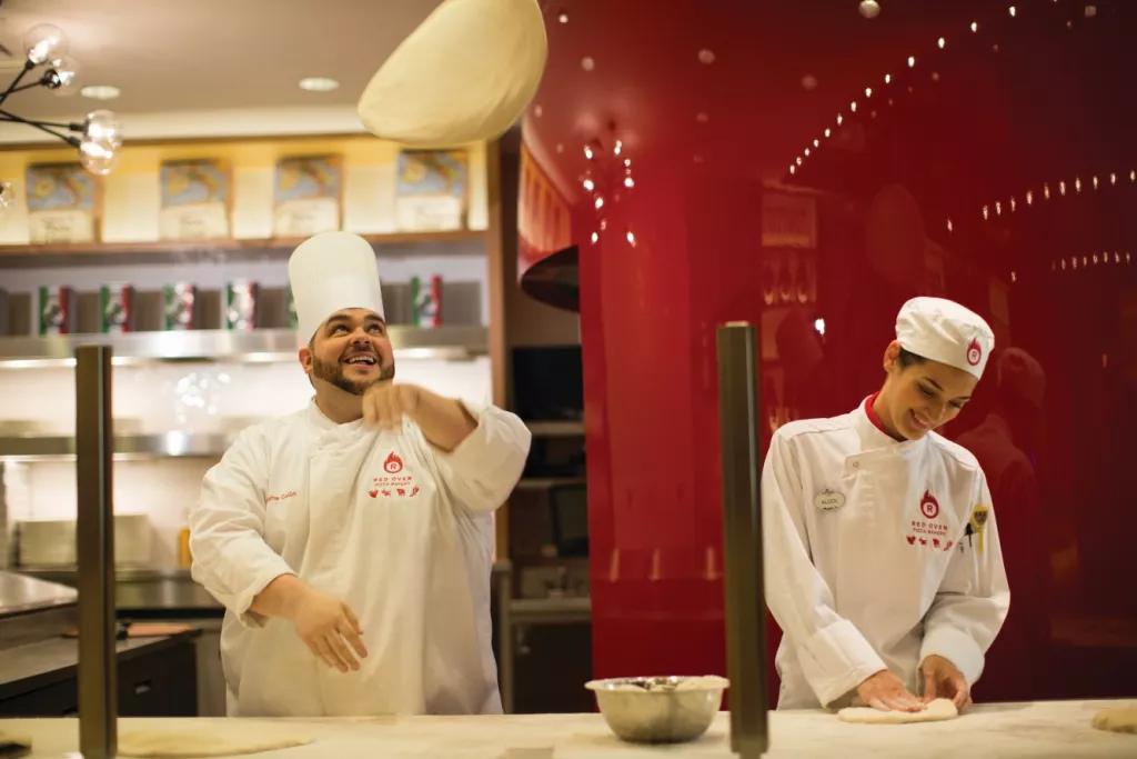 Two chefs standing at a bench tossing pizza dough