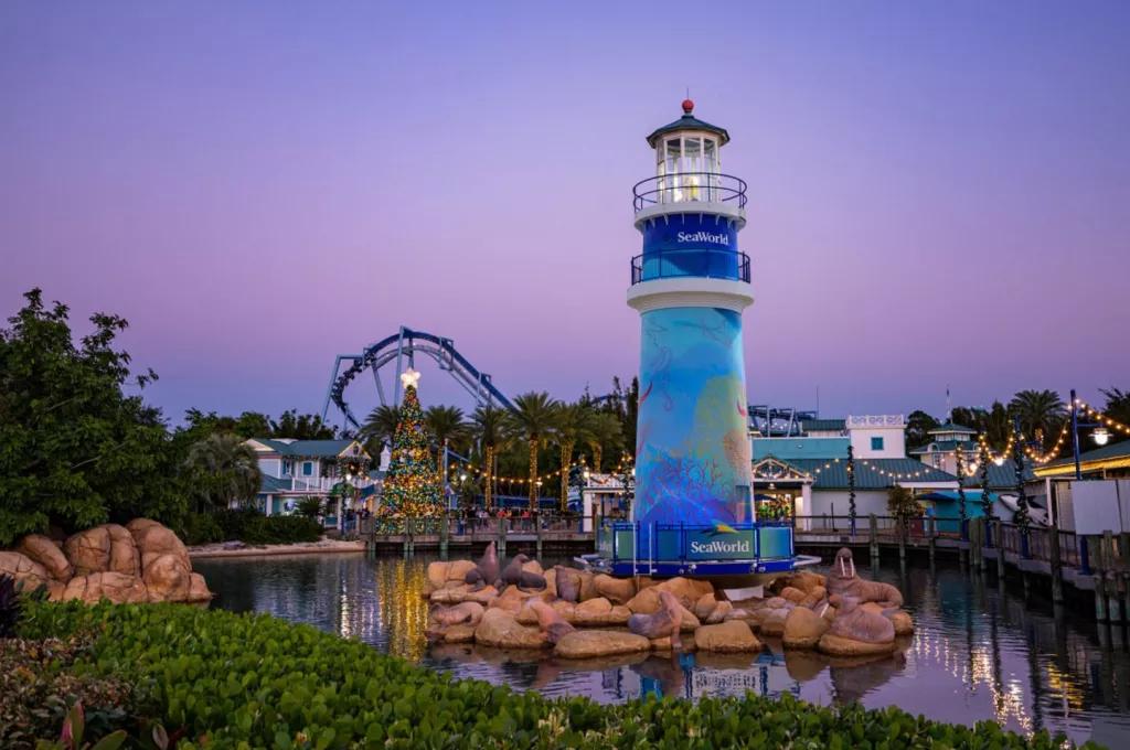 The SeaWorld lighthouse in front of a purple tinted sky and a lit up Christmas tree