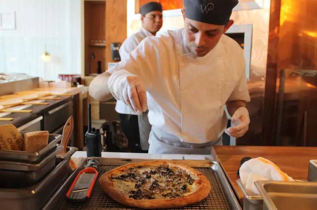A chef sprinkling cheese onto a pizza