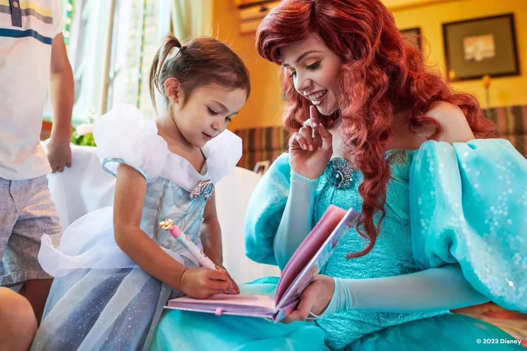 A child in a Cinderella costume drawing in a book held by Ariel
