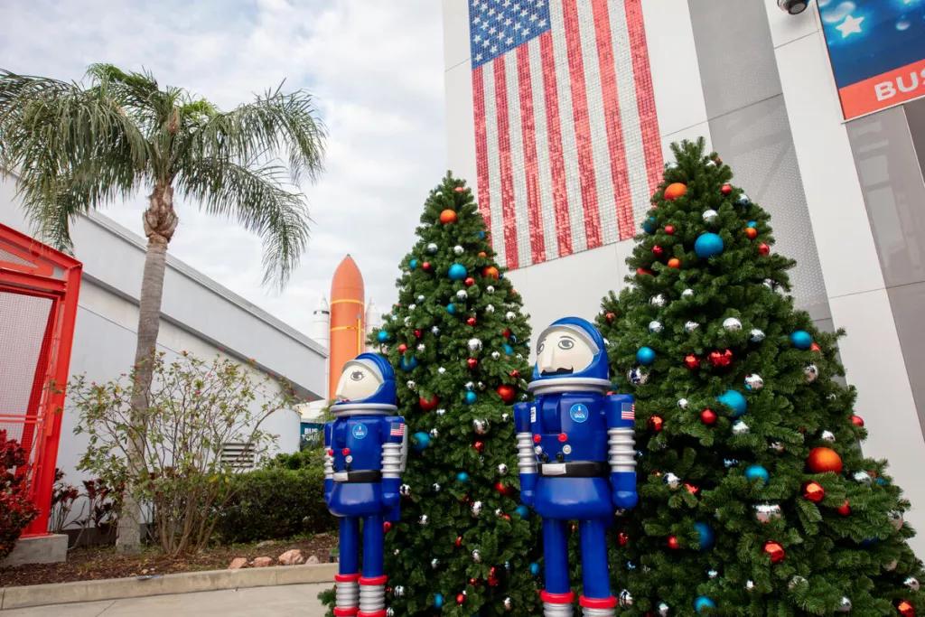 Large astronaut themed nutcrackers in front of Christmas trees and a building with an American flag