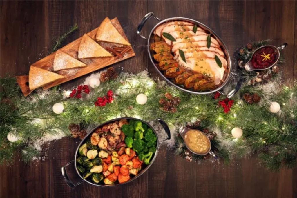 A bird's eye view of a table decorated for Christmas with plates of turkey, stuffing, roasted vegetables and pie. 