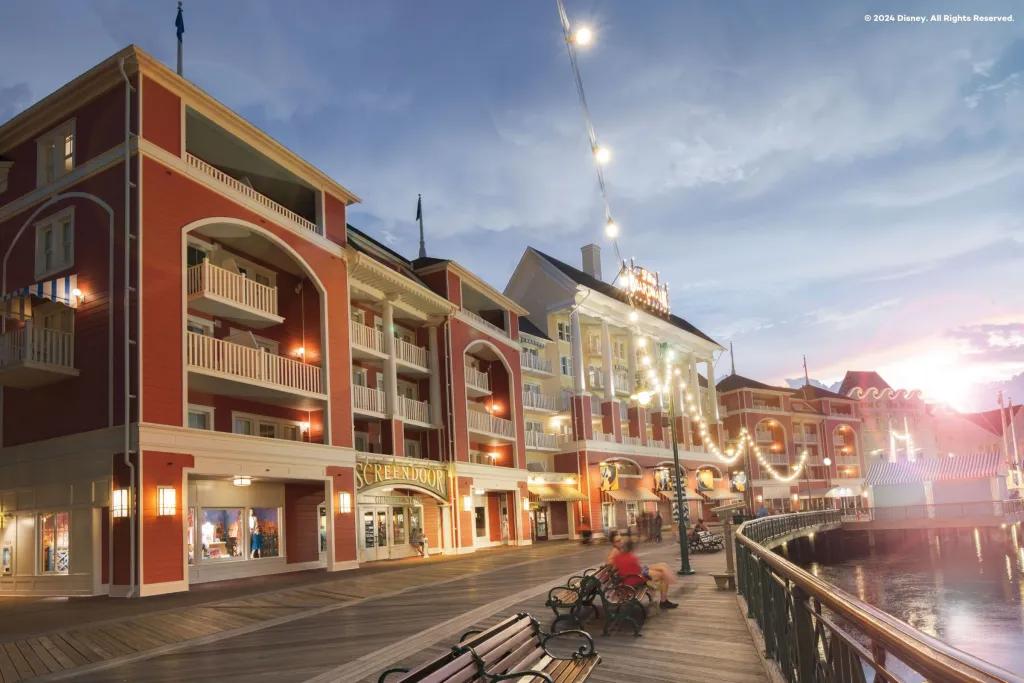 A wooden boardwalk in front of a row of multicoloured buildings lit with fairy lights 