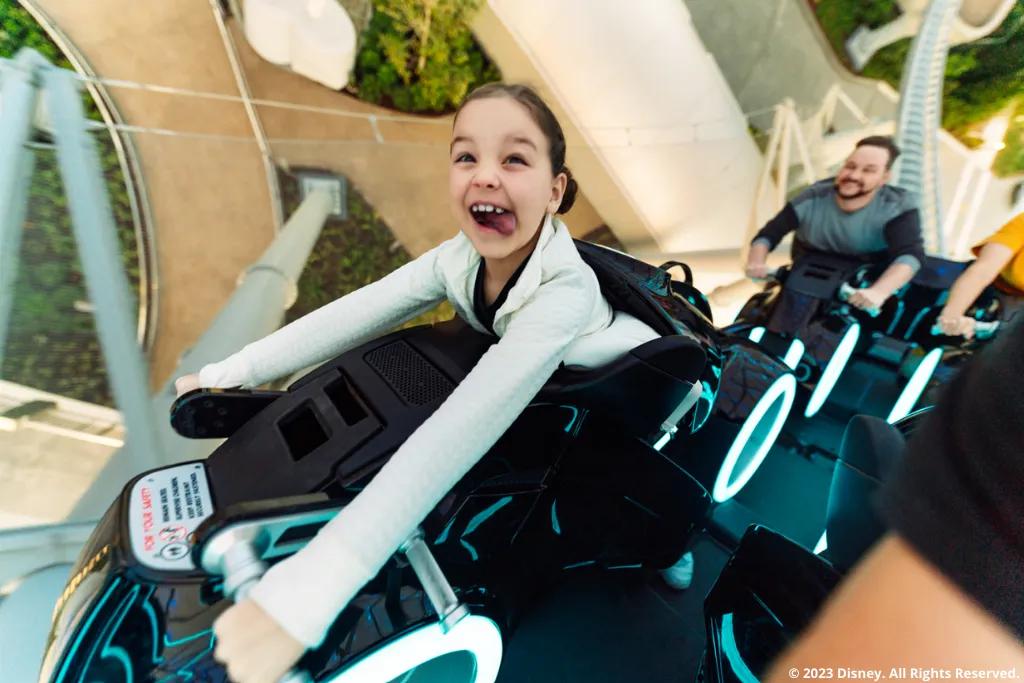 Ein Kind fährt die neue Magic Kingdom Park Attraktion TRON Lightcycle / Run und streckt die Zunge heraus
