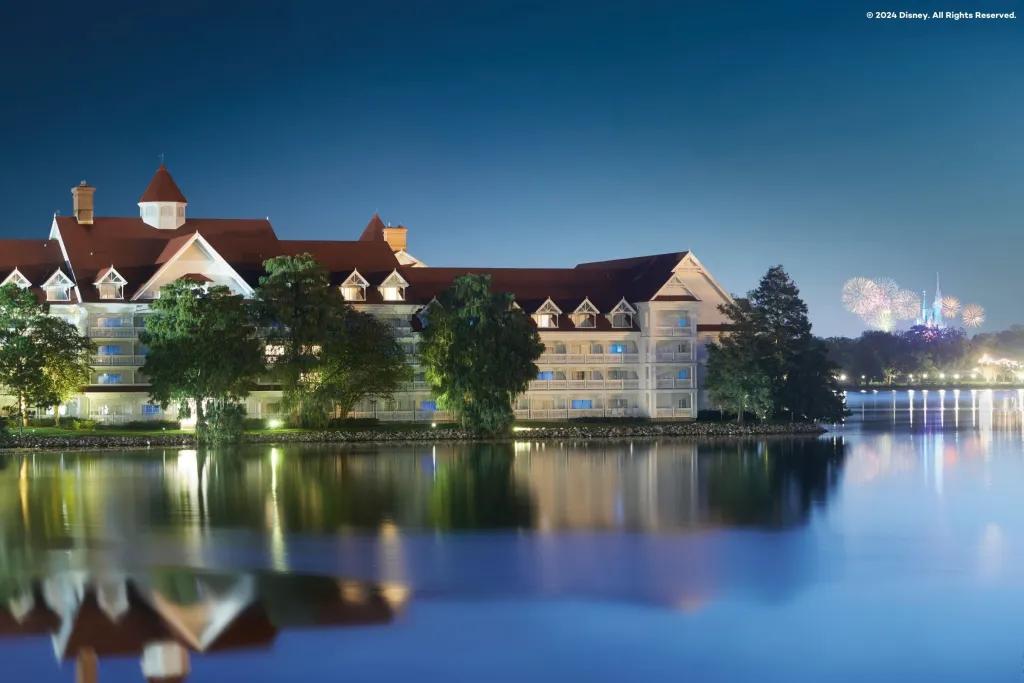 Looking across a lake to a Victorian style building and a castle surrounded by fireworks in the background