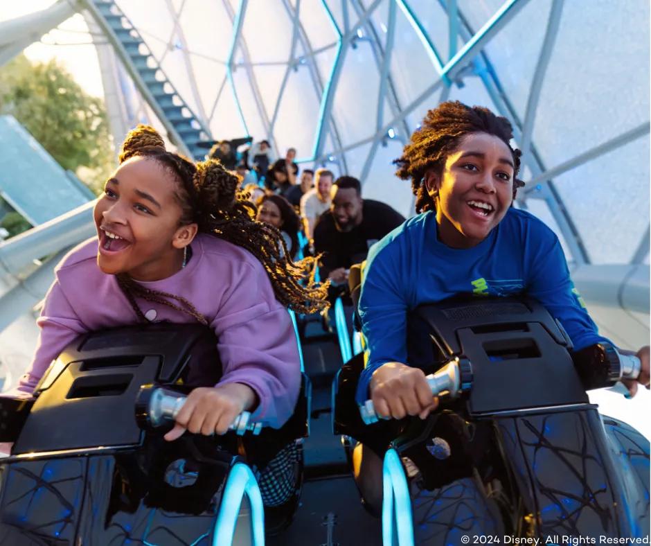 Two guests smiling as they are launched, sat on bike shaped vehicle riding TRON Lightcycle/Run