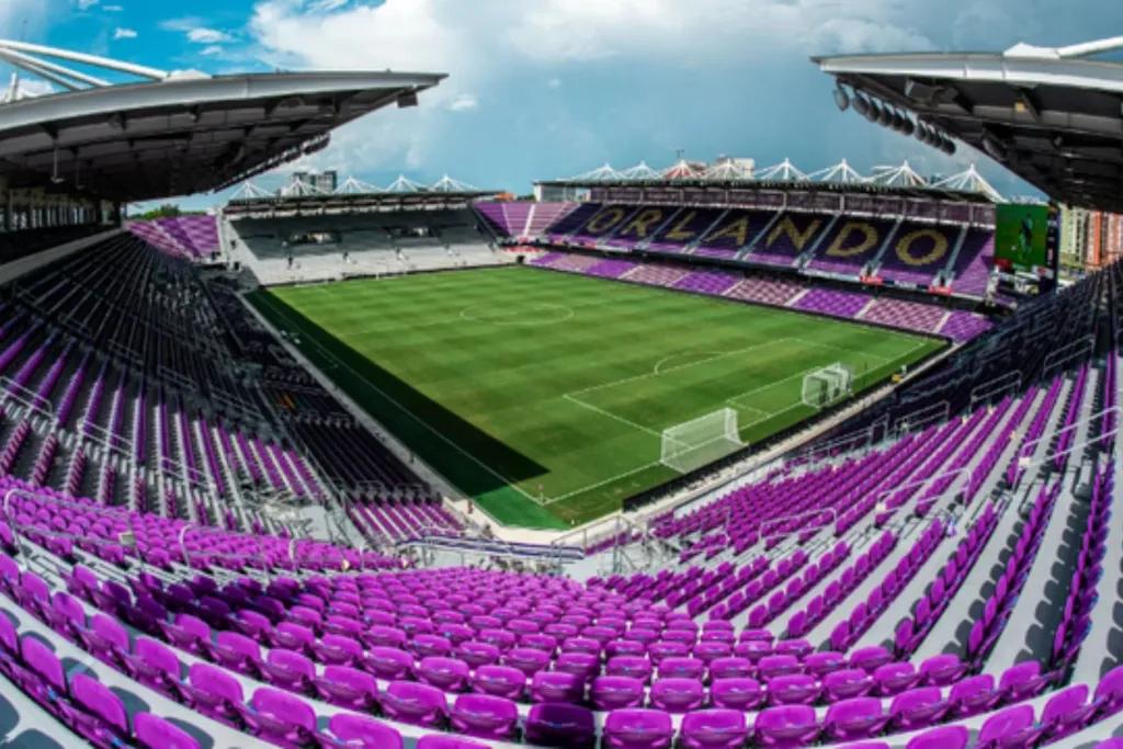 Looking down into an empty football stadium with purple seats. The pitch is empty