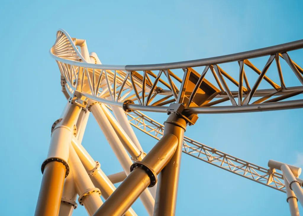 Looking up at a golden coloured rollercoaster track in front of a clear blue sky