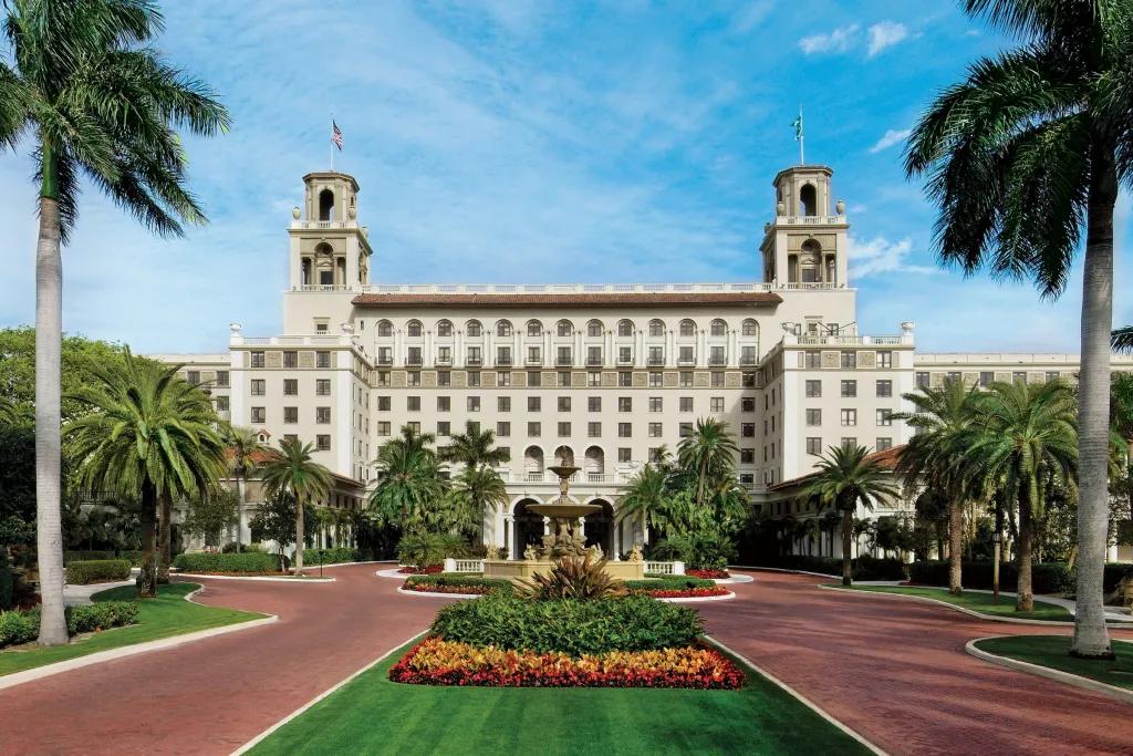 A large palm tree-lined driveway leading up to a grand hotel building