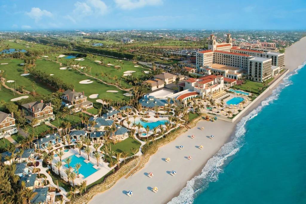 Aerial view of a hotel complex along a strip of private beach leading up to bright blue sea water