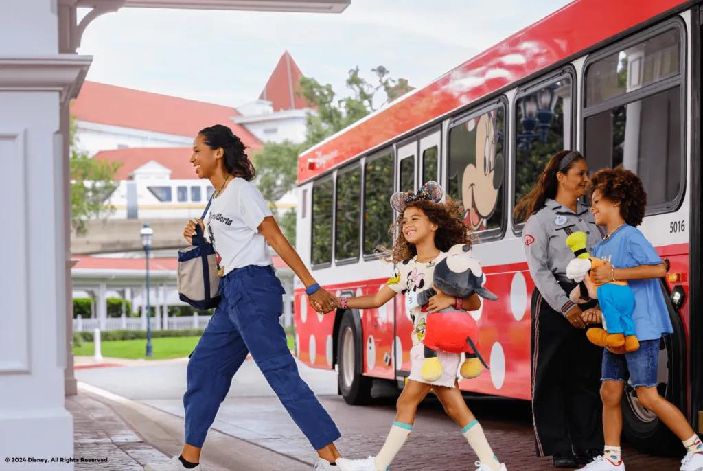 A woman leading a young girl and young boy off a bus decorated with polka dots
