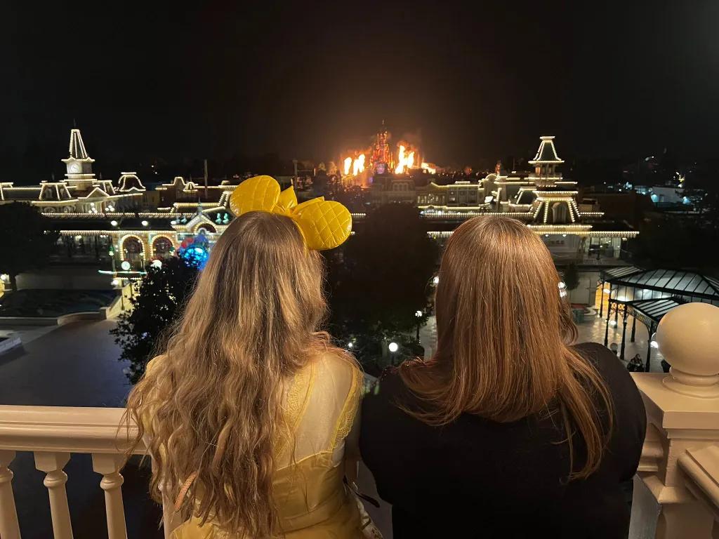 Two women facing away from the camera watching a fireworks display at a Disney park 