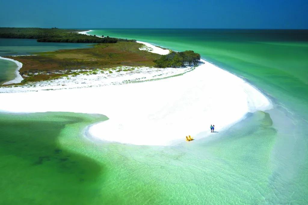 Two yellow deck chairs and a couple walking along white sandy beach of deserted island. 