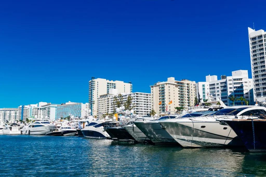 Yachts and boats docked in harbour with the Miami skyline in the background, lots of tall buildings.