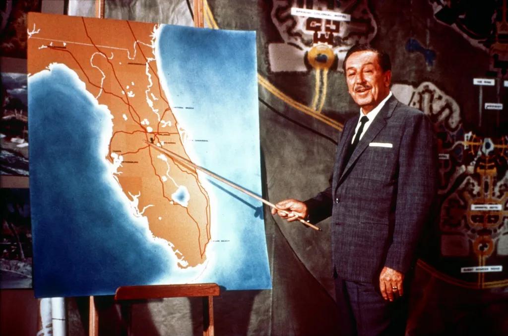 Walt Disney stood in front of colourful map of Florida with wooden stick to point for television broadcast.