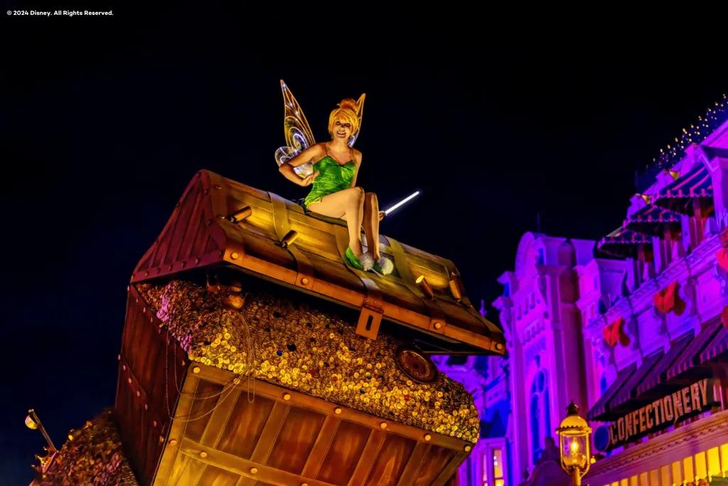 Tinkerbell sitting on top of a open chest of gold on a parade float 