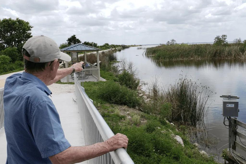An old man looking out at a swamp and pointing into the distance