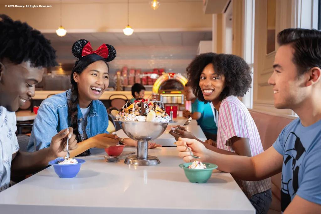 A group of friends sat round a table in a diner eating a giant ice cream sundae