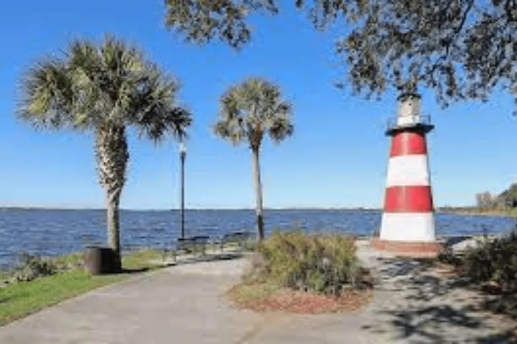 A white and red striped lighthouse and palm trees in front of a lake