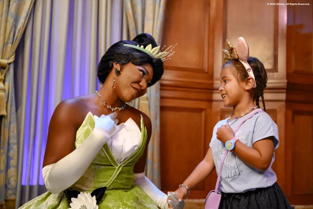 A young girl wearing pink Minnie Mouse ears holding hands with Princess Tiana 
