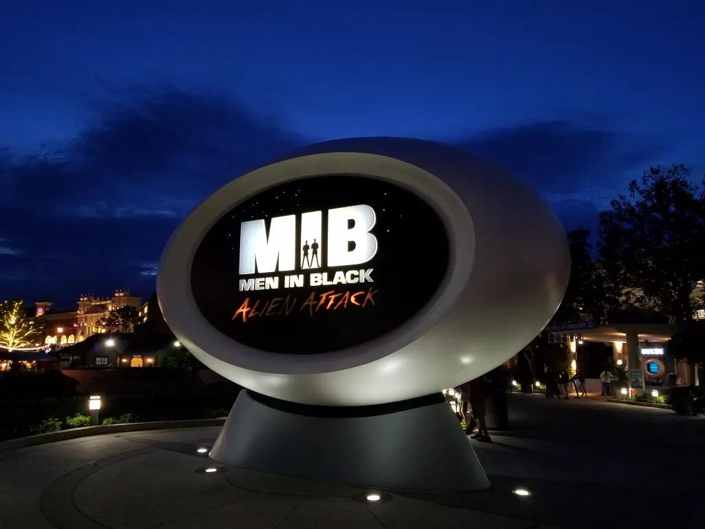 Dark sky in the background with blue hue, with a sign saying "M.I.B. Men in Black Alien Attack"