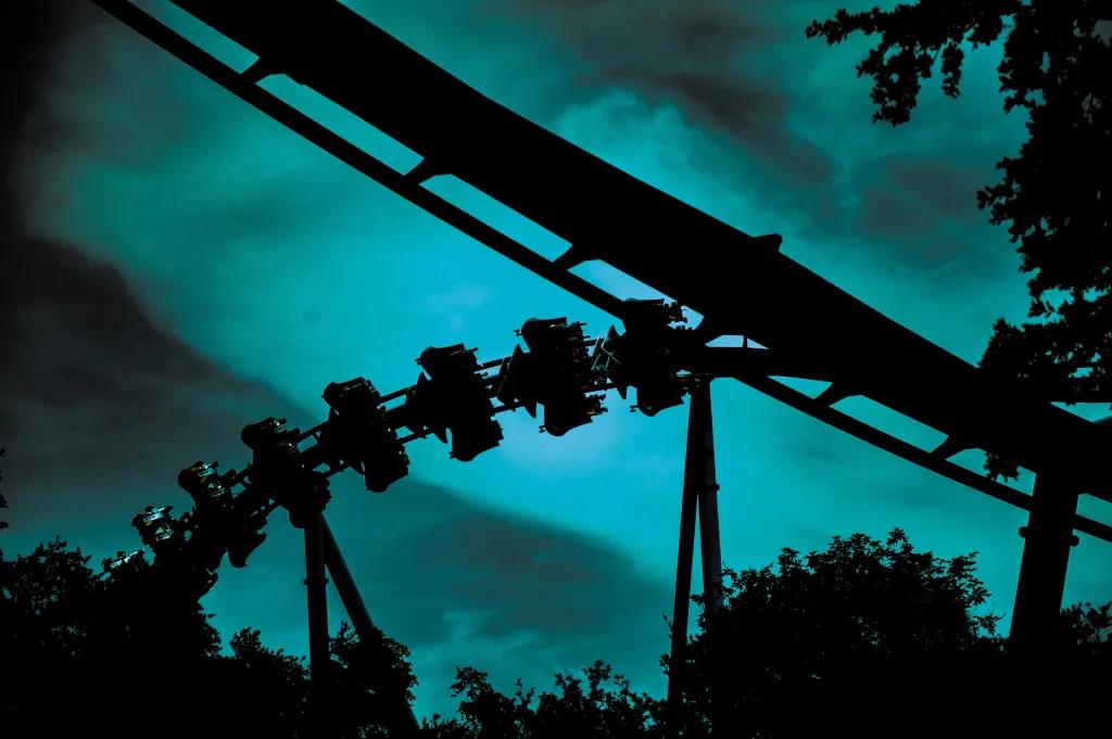 Dark night sky with streaks of turquoise light which outline the silhouette of manta roller coaster flying through track.