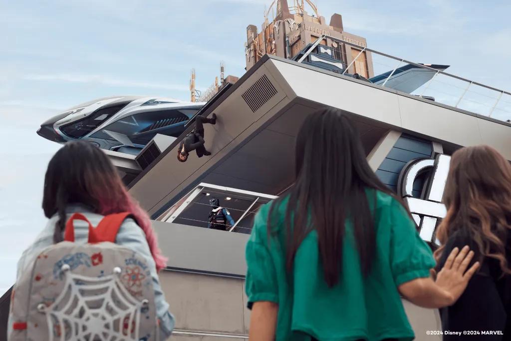 Three women looking up to superheroes scaling a building at Avengers Campus
