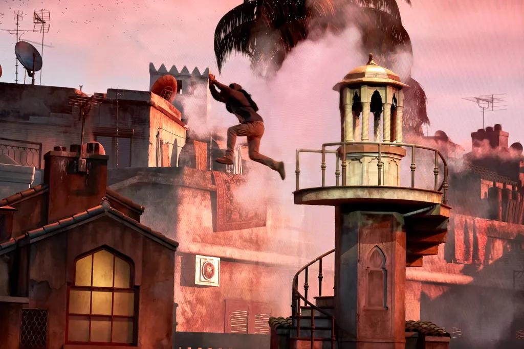 There are buildings and a palm tree in the background. There is a man leaping through the sky high up off of a tower with a spiral staircase. There is also smoke in the background.
