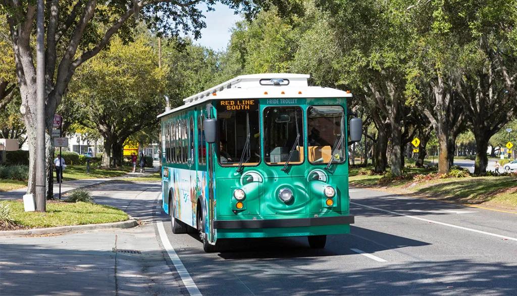 A green bus driving on a road with a cartoon face on the front smirking and looking off to the side. 