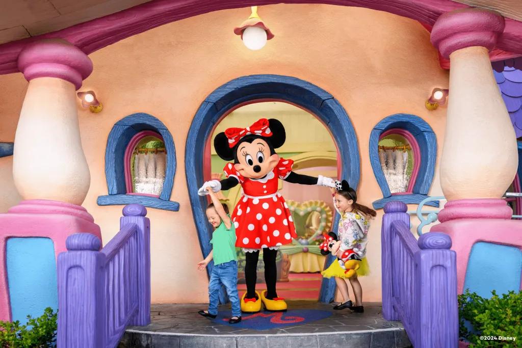 Two young girls dancing with Minnie Mouse on the steps of her house at Disneyland 